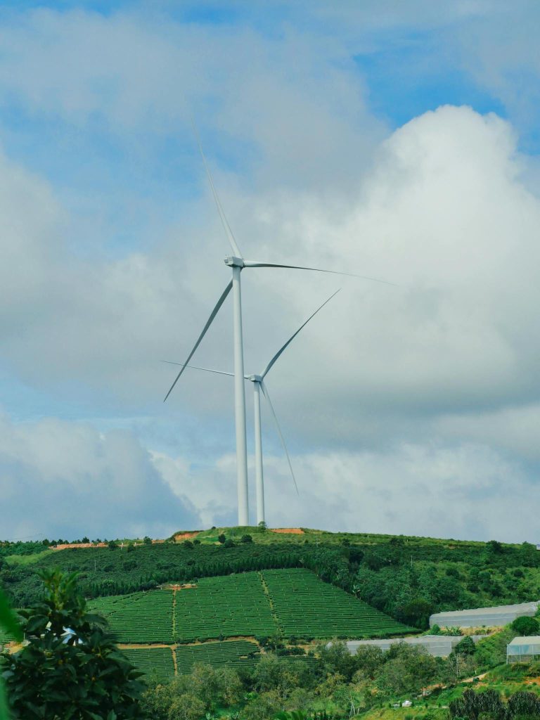 Wind turbines on a green hill in Đà Lạt, Vietnam against a cloudy blue sky.